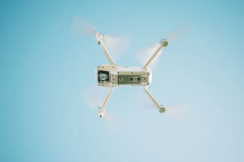 A white delivery drone hovering in a pale blue sky