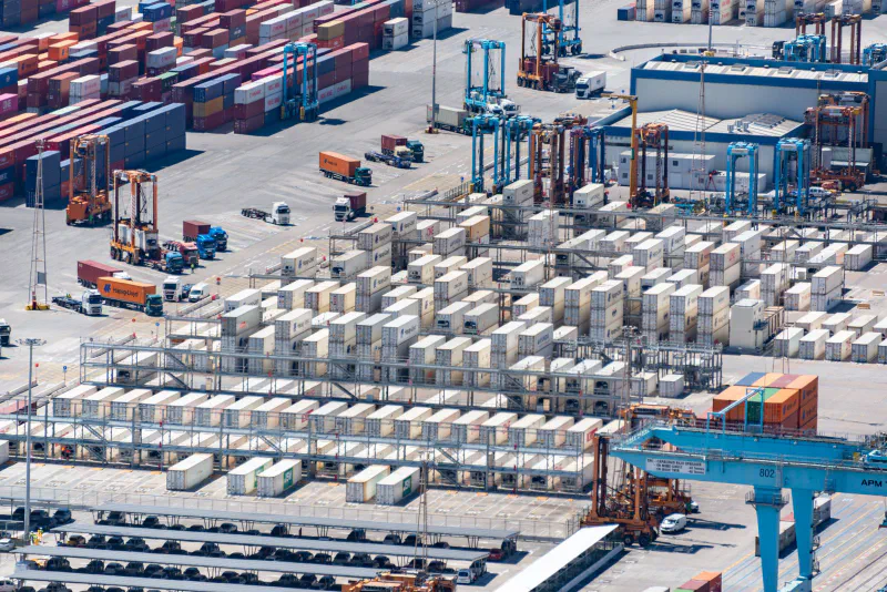 Aerial view of a container port yard with stacked shipping containers and cranes