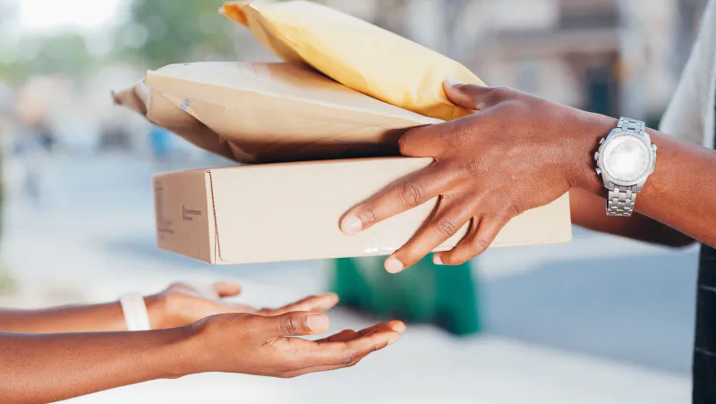Hands passing several small parcels and padded mailers to another person