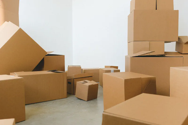 A group of plain brown cardboard shipping boxes in many different sizes on a floor against a white wall