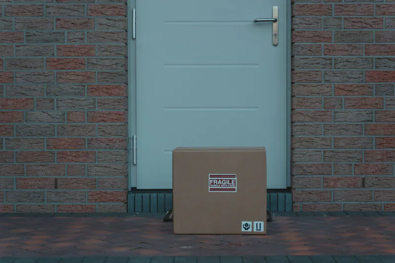 A brown cardboard delivery box left on a doormat in front of a house door