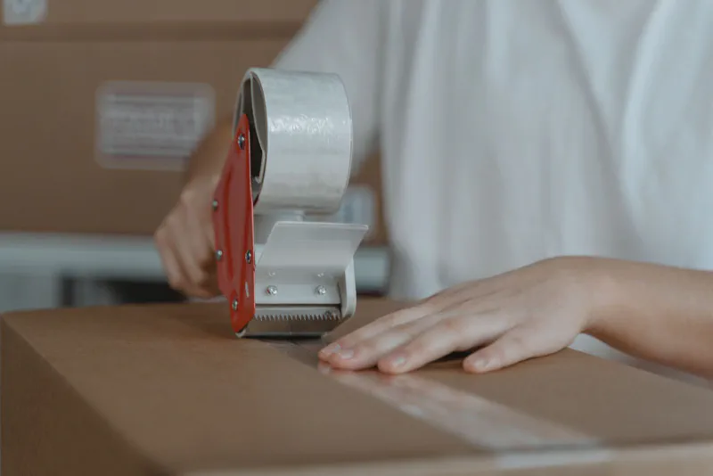 Hands sealing a cardboard box with a tape gun