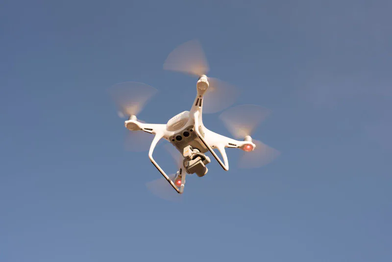 A white quadcopter delivery drone flying against a clear blue sky