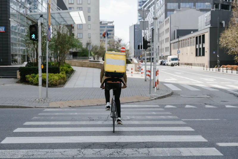 A bicycle courier with a delivery box riding across a city crosswalk, seen from behind