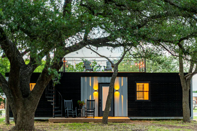 A black and white shipping container converted into a tiny home with a rooftop deck among trees