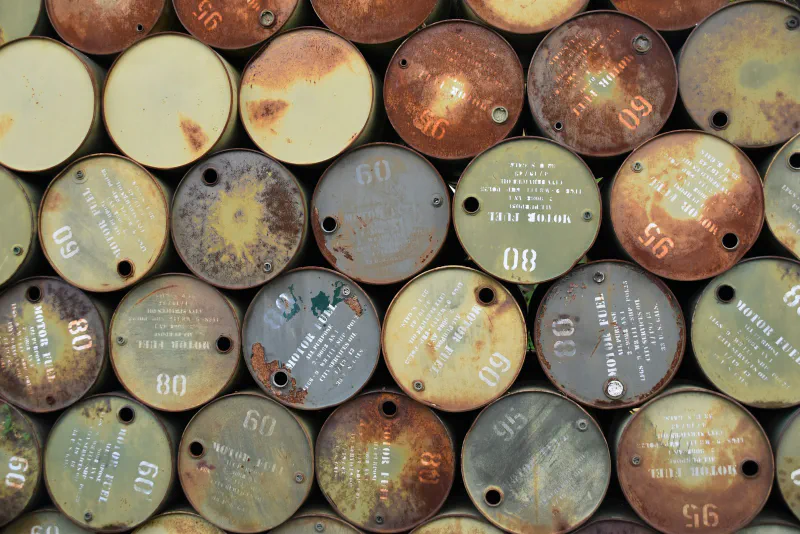 Stacked metal fuel drums viewed from their ends, showing stenciled markings and rust