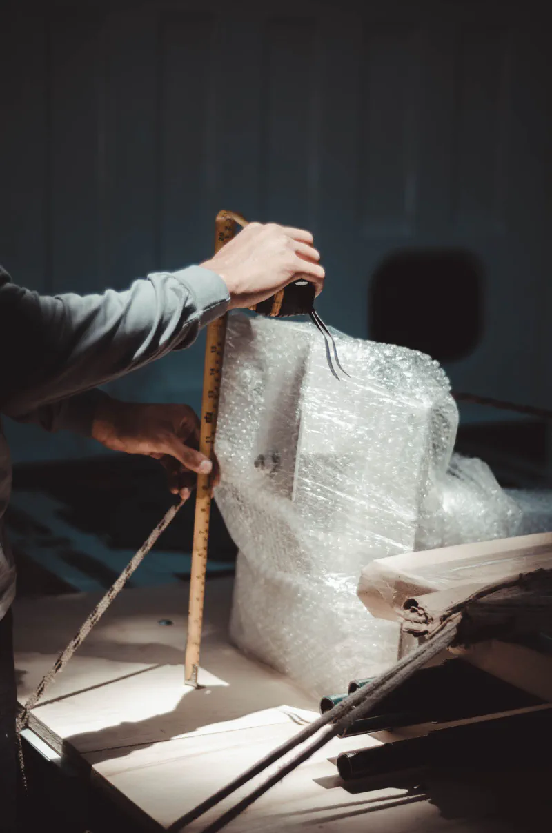 A hand holding a folding ruler against a bubble wrapped package to measure its dimensions