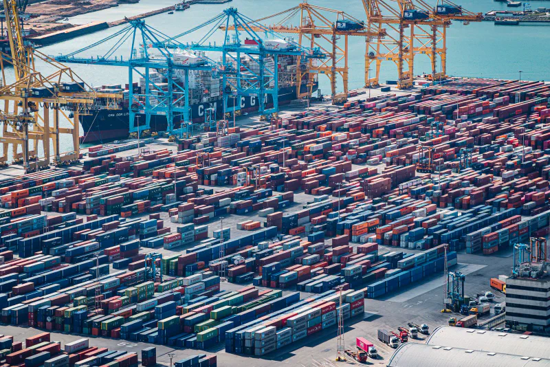 Aerial view of a container port with thousands of stacked shipping containers, cranes, and a cargo ship